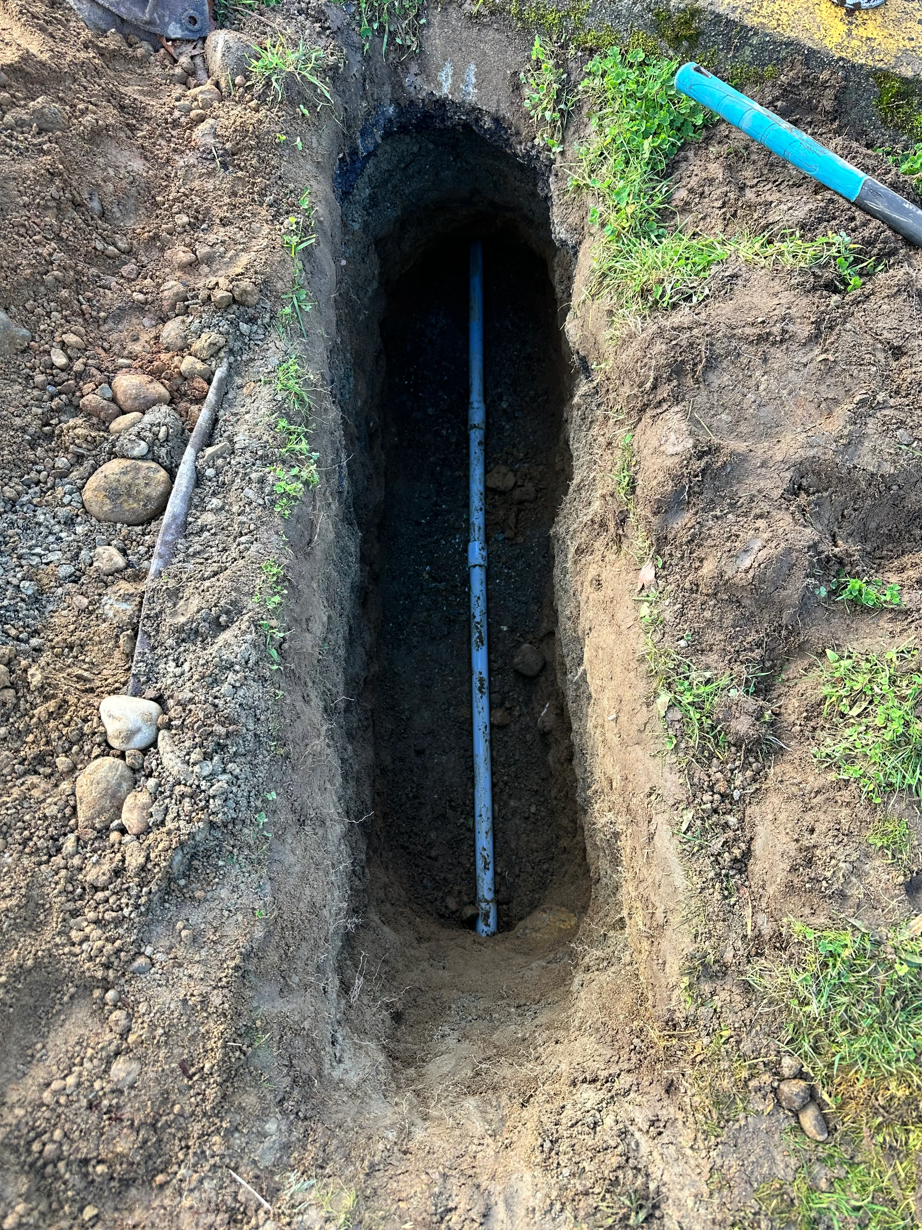 Blue PVC utility line installed in excavated underground trench with gravel base